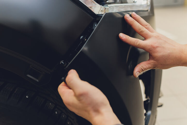 Auto body repair school graduate inserting new bumper on vehicle