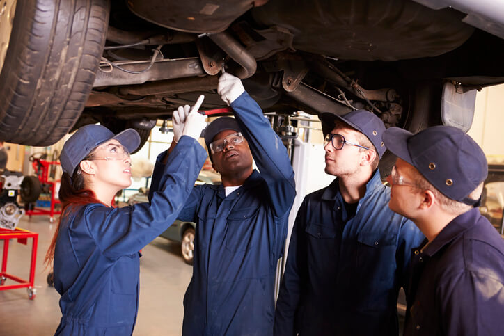 A group of students in diesel mechanic training working as apprentices inspecting under a vehicle.