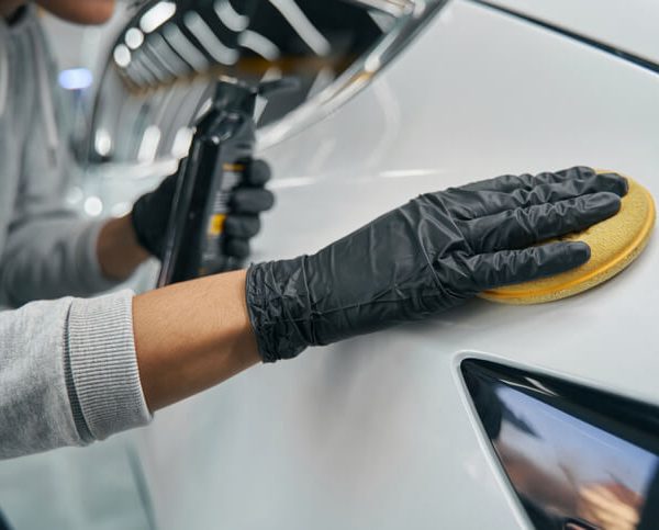 A freelance auto detailer applying a treatment to the vehicle exterior after auto detailing training.