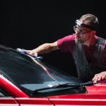 A male professional auto detailer polishing a car's windshield