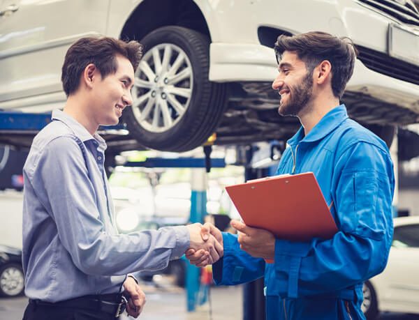 A service advisor training graduate shaking hands with a customer in a garage