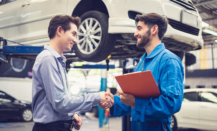 A service advisor training graduate shaking hands with a customer in a garage