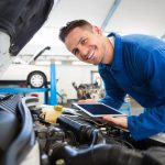 A smiling male auto mechanic using technology to diagnose a car's engine after graduating from auto mechanic school