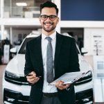 An auto sales training grad wearing a suit posing in a dealership