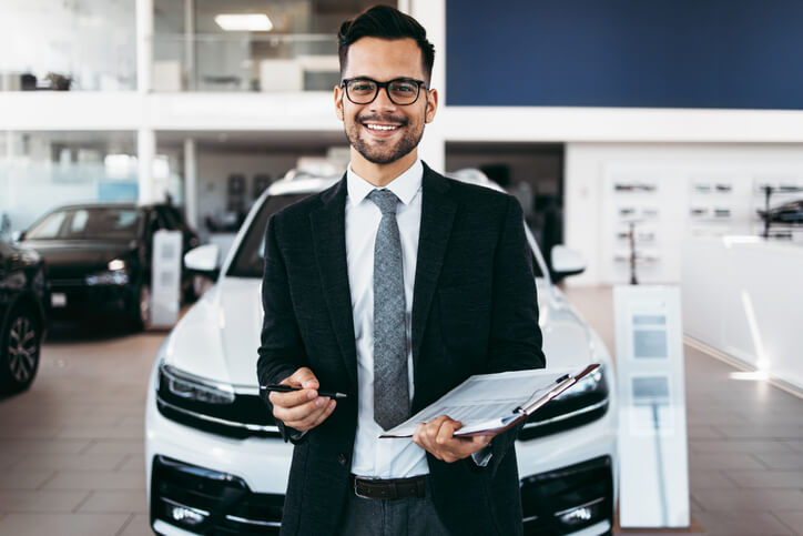 An auto sales training grad wearing a suit posing in a dealership