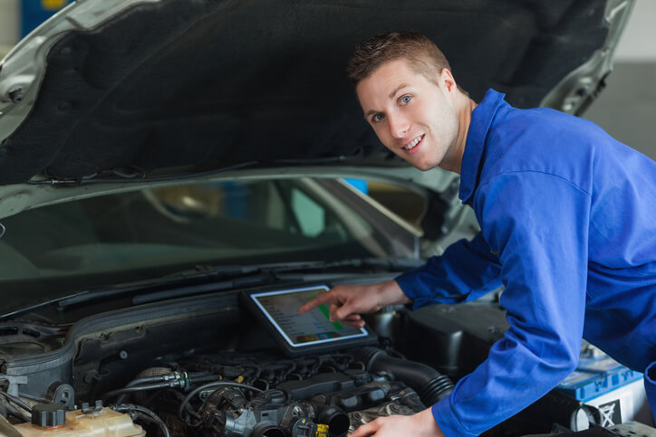 A smiling auto mechanic working on a vehicle's engine after graduating from auto mechanic school