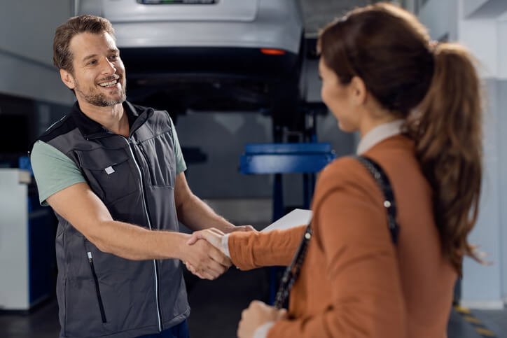 A smiling male auto mechanic greeting his customer at an auto repair shop after his automotive training