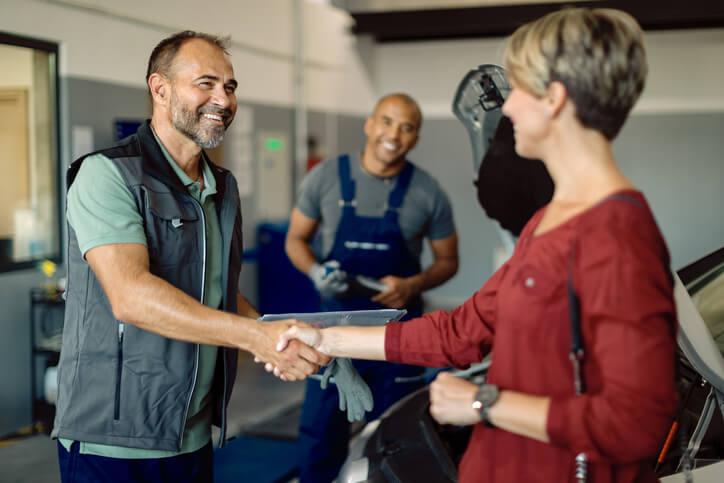 A happy auto mechanic shaking the hands of a female customer after completing his automotive training