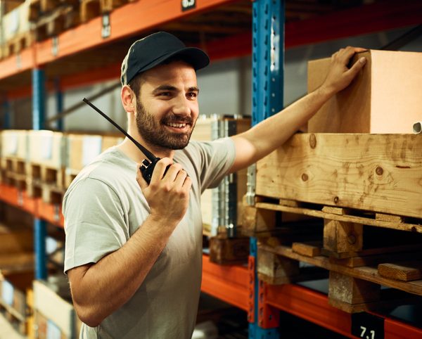 A smiling dispatcher holding a walkie-talkie in a warehouse, using radio language codes learned during dispatch training