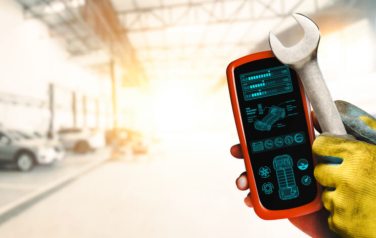 An automotive training student holding an OBD 2 scanner and a wrench
