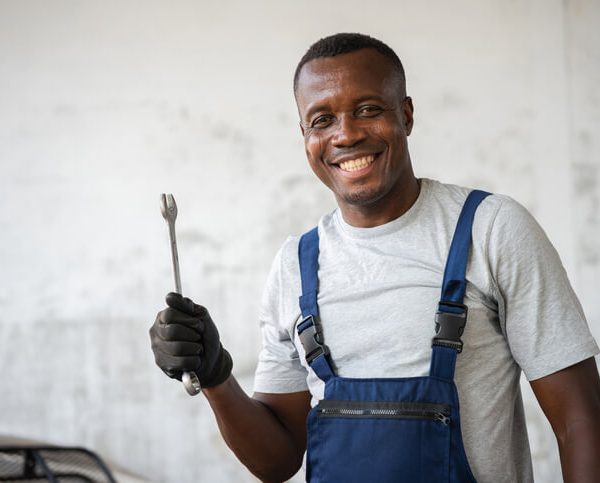 A smiling auto mechanic holding a wrench in a garage, representing automotive careers.