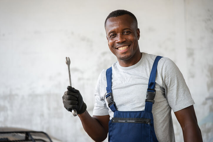 A smiling auto mechanic holding a wrench in a garage, representing automotive careers.
