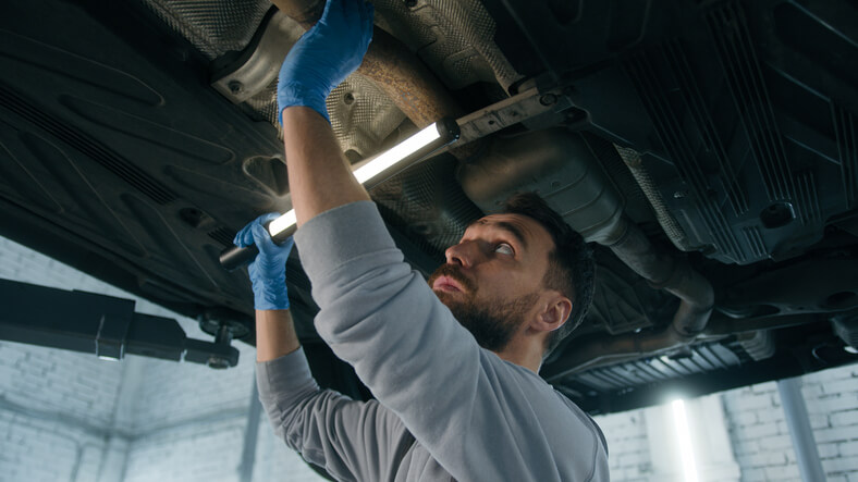 A student practicing exhaust system diagnostics as part of auto mechanic training.