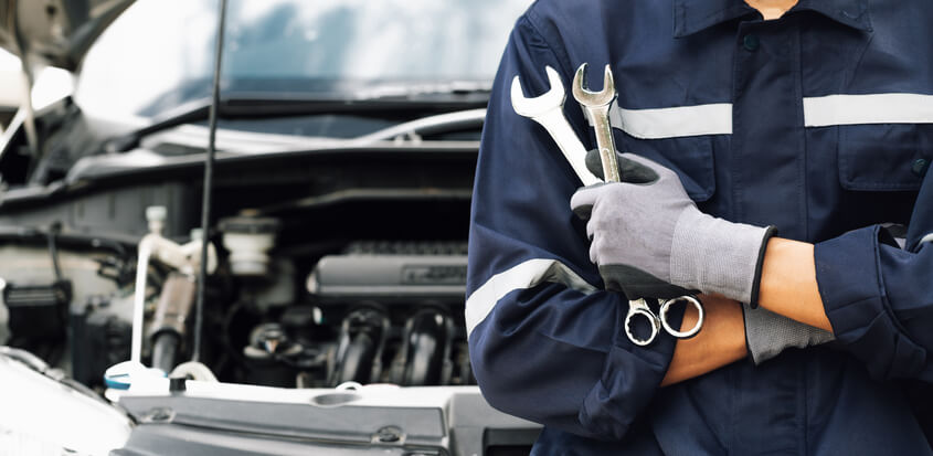 An auto mechanic training student working with wrenches at an auto repair shop