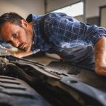 A student listening to a car engine with a stethoscope in a dimly lit garage.