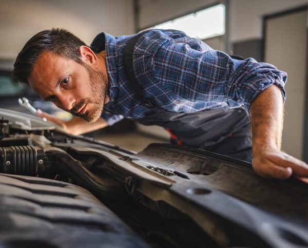 A student listening to a car engine with a stethoscope in a dimly lit garage.