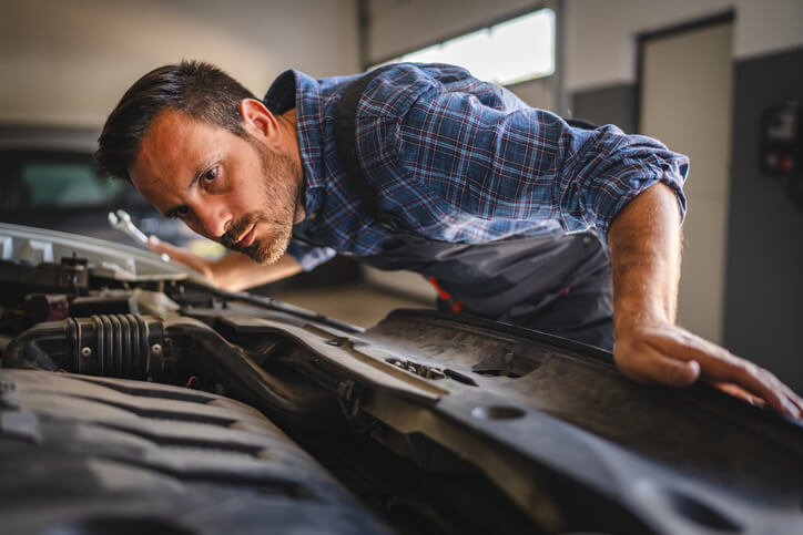 A student listening to a car engine with a stethoscope in a dimly lit garage.