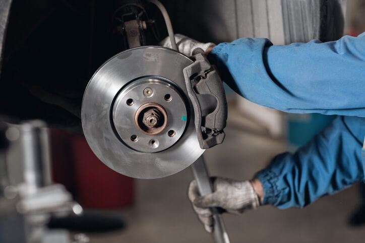 A technician examining a brake rotor on a vehicle hoist during hands-on automotive training.