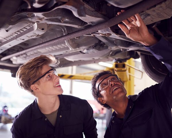 A student in auto mechanic training working on an engine with an instructor nearby, highlighting a learning moment.