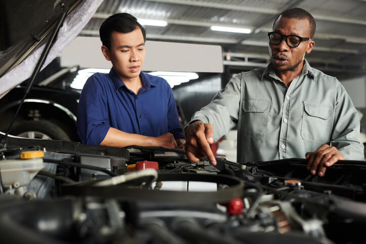 An automotive training student is inspecting an engine with an instructor.