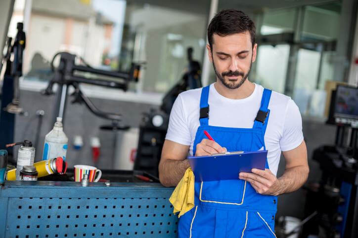 A mechanic-in-training reviewing a checklist after a minor workshop mistake, focused on improvement.
