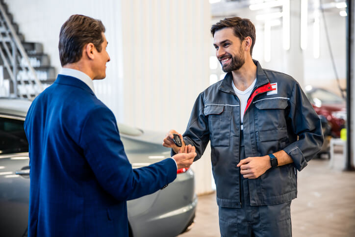 An auto mechanic training graduate hands car keys to a customer after completing vehicle service at a garage.