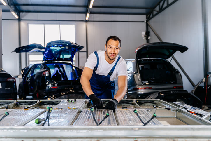 A technician in protective gloves is handling an EV battery pack in a workshop as part of EV battery recycling and safe removal procedures.