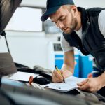 An entry-level mechanic performing a safety check in a busy auto shop in 2026.