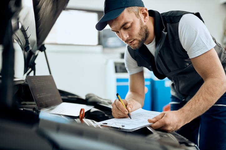 An entry-level mechanic performing a safety check in a busy auto shop in 2026.