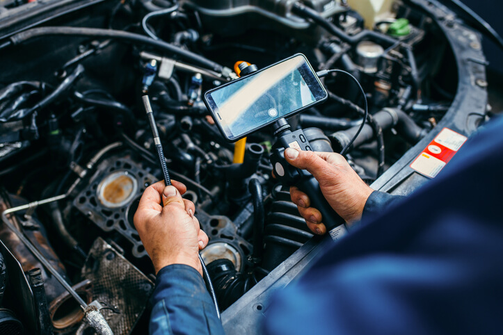 An auto mechanic training technician is inspecting intake valves using a borescope