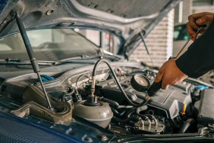 A technician performing an engine compression test using a pressure gauge