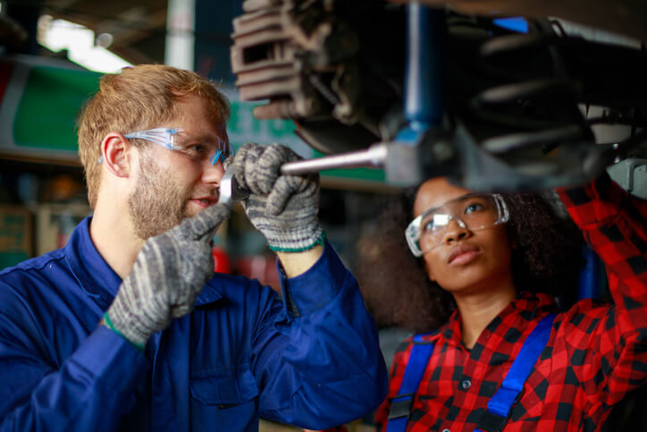 A trainee learning to use automotive tools in a mechanic apprenticeship workshop