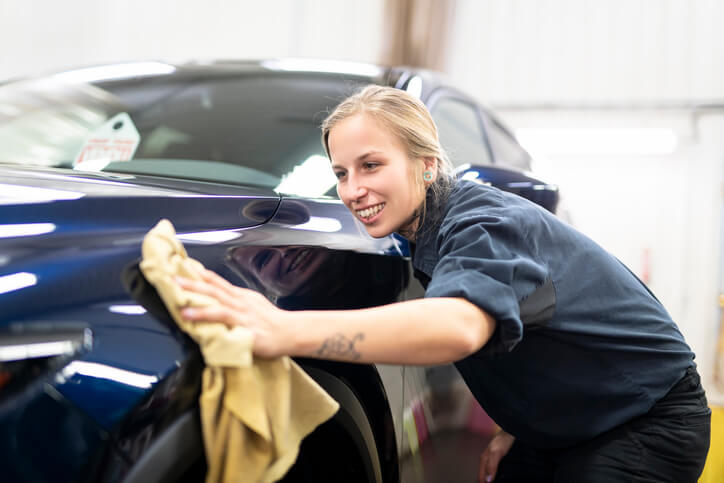 An automotive student performing paint correction polishing in a detailing workshop