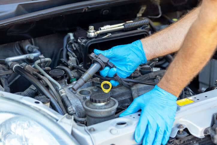 A mechanic testing the ignition coil electrical output in a vehicle engine bay