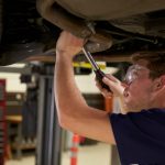 Automotive student inspecting a vehicle exhaust system on a service lift