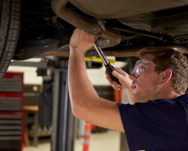 Automotive student inspecting a vehicle exhaust system on a service lift