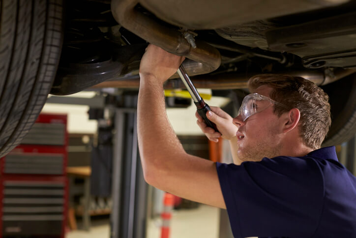 Automotive student inspecting a vehicle exhaust system on a service lift