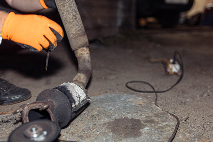 Technician examining a rusted muffler with visible holes during an inspection