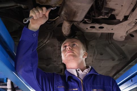 Automotive training student checking exhaust components underneath a vehicle
