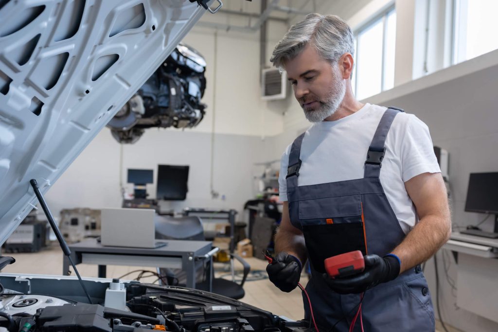 Technician inspecting starter and battery connections in an automotive workshop