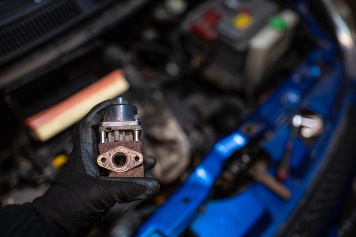 A mechanic inspecting an EGR valve for carbon buildup and sticking