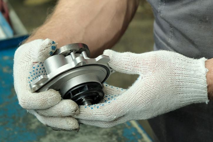A technician checking a water pump for signs of coolant leakage