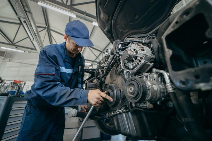 A technician checking serpentine belt alignment during an engine inspection