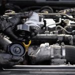 An automotive technician inspecting a serpentine belt tensioner in an engine compartment